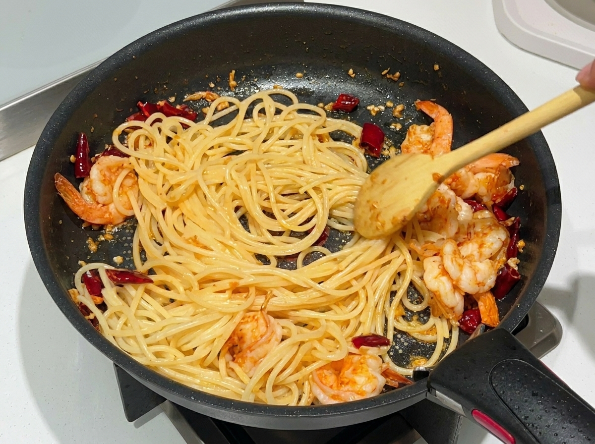 フライパンの中のパスタにオイスターソースを加え、混ぜ合わせている様子。