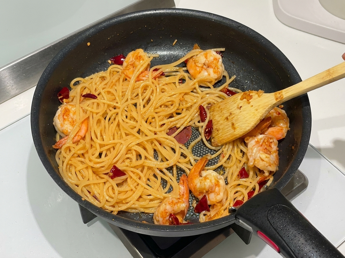 パスタと海老をフライパンの中で手際よく煽り、全体を馴染ませている様子。