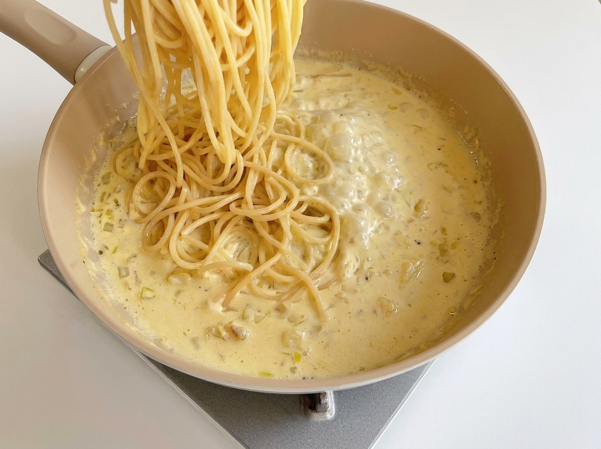チーズソースに茹でたスパゲッティを加えている様子
