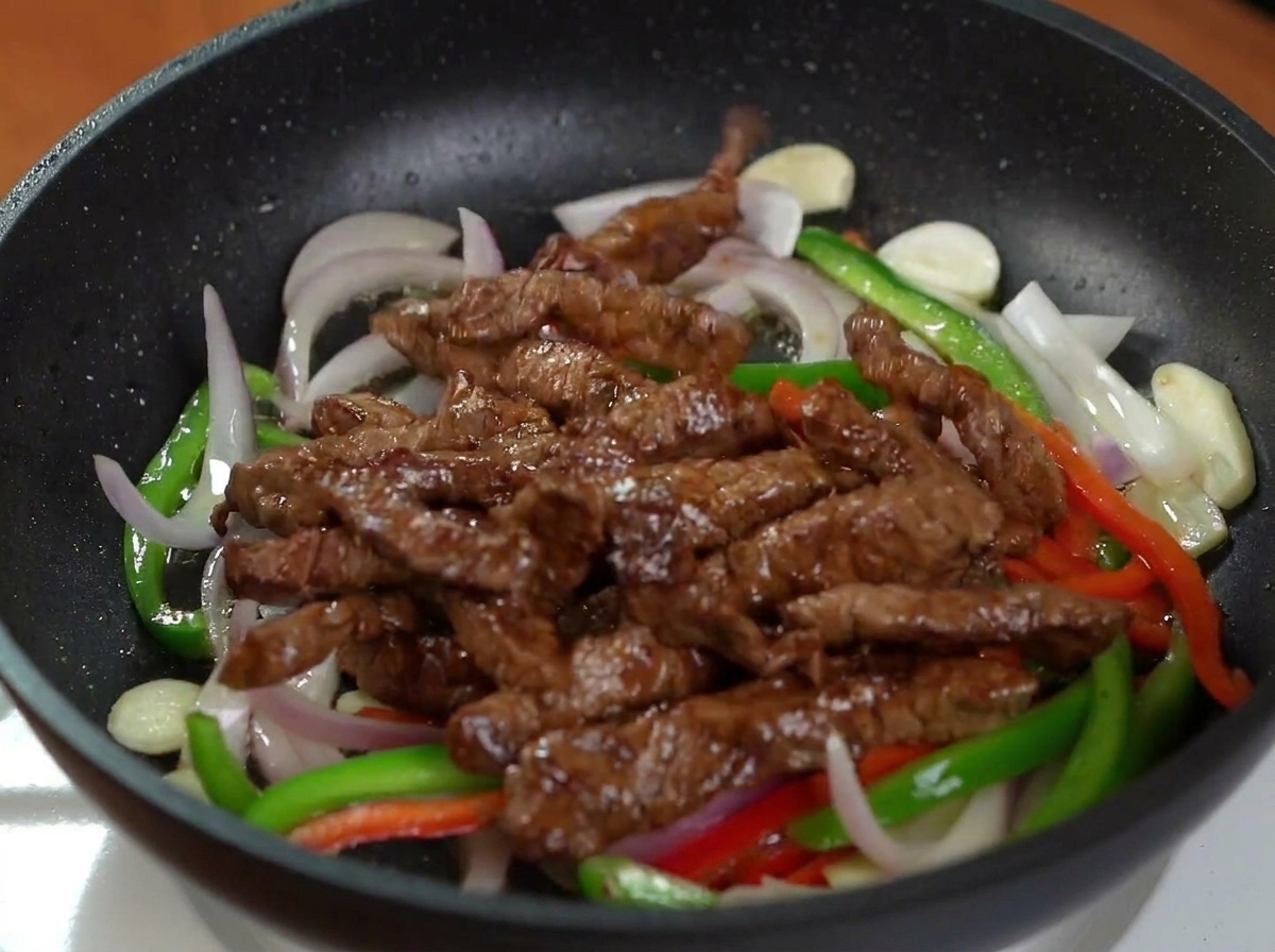 野菜が炒められたフライパンに、先ほど焼いた牛肉を戻し入れた様子。