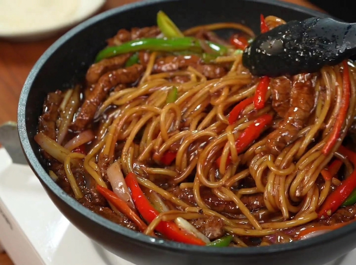 お皿に盛り付けられたパスタ、牛肉、ピーマンの上に、刻んだパセリが散らされている様子。