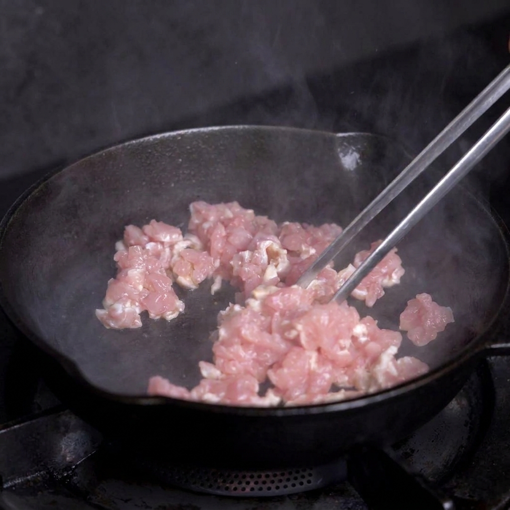 熱したスキレットで、角切りの赤身肉をトングを使って炒めている様子。