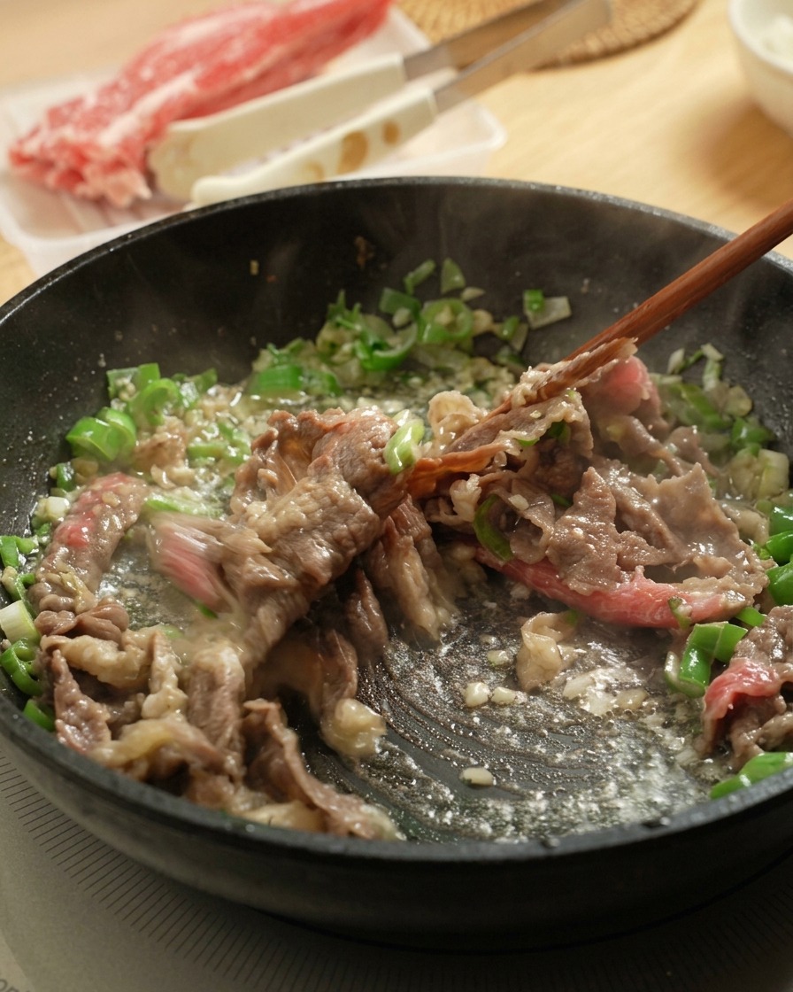 箸を使ってフライパンの中の牛肉をほぐしながら炒める様子。