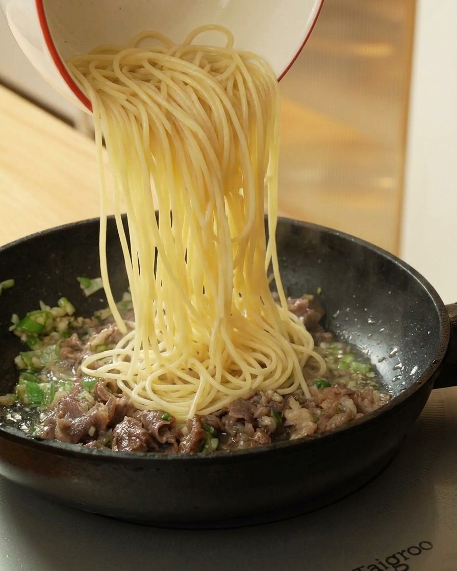 牛肉が入ったフライパンに、茹でたスパゲッティを加える様子。