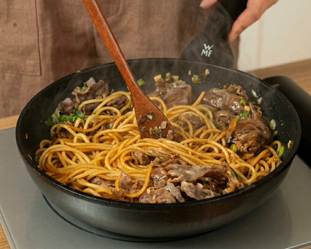 ヘラを使い、麺と肉にソースを絡めながら勢いよく炒める様子。