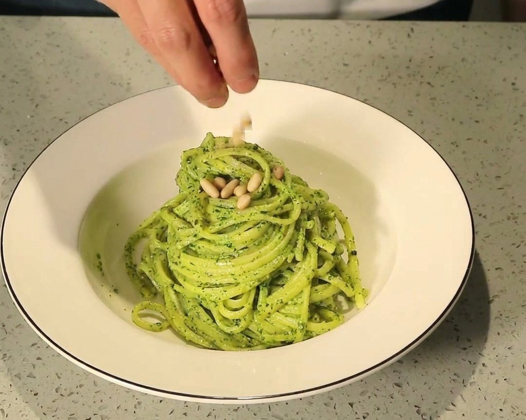 お皿に盛り付けたパスタの上に、ローストした松の実を散らしている様子。