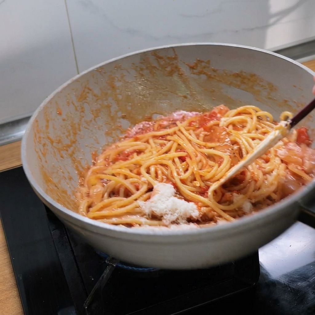 フライパンを振り、ソース、パスタ、チーズを一体化させてツヤを出している様子。