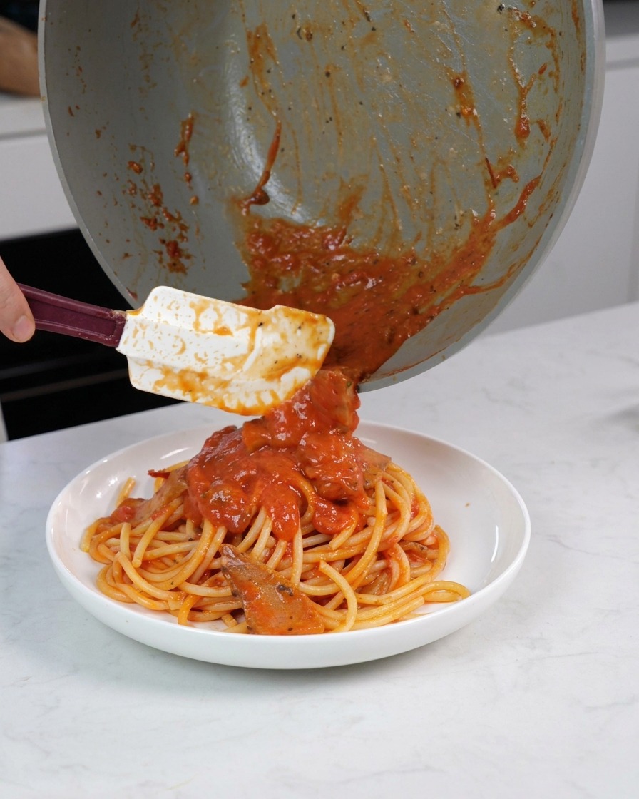 お皿に盛ったパスタの上に、フライパンに残った具材たっぷりのソースを丁寧にかけている様子。