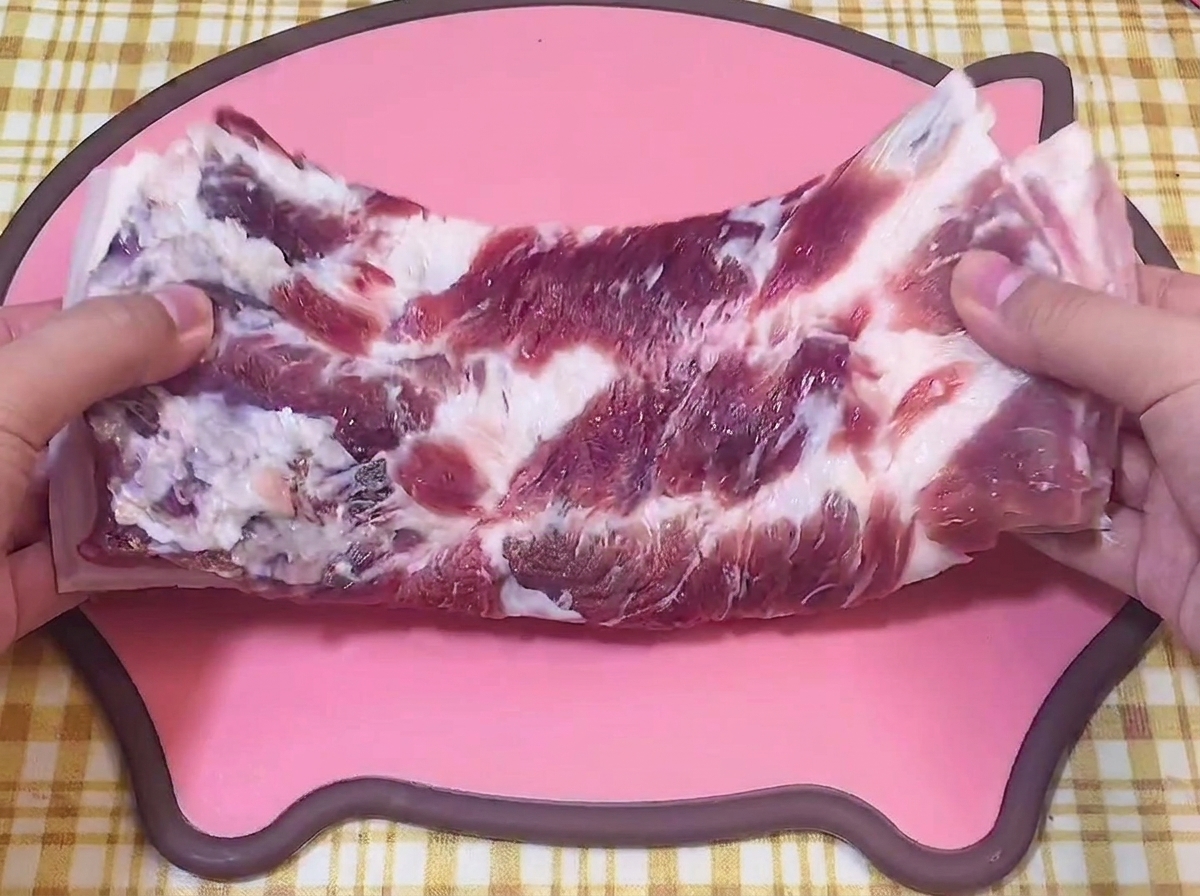 豚の形をしたピンクのカッティングボードの上で、生の豚バラ肉を手に持っている様子。