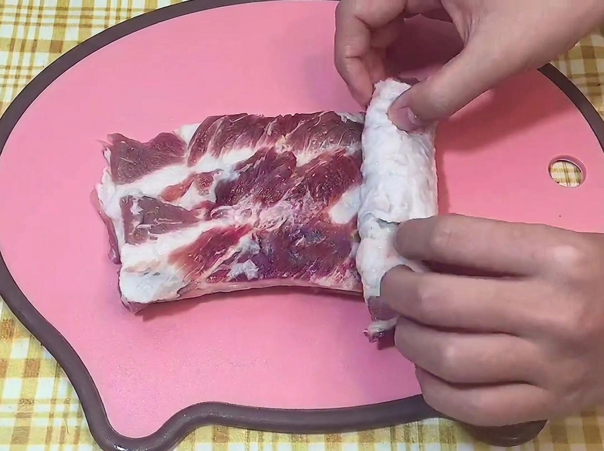まな板の上で、切り込みを入れた生の豚バラ肉をきつく円柱状に巻いている様子。