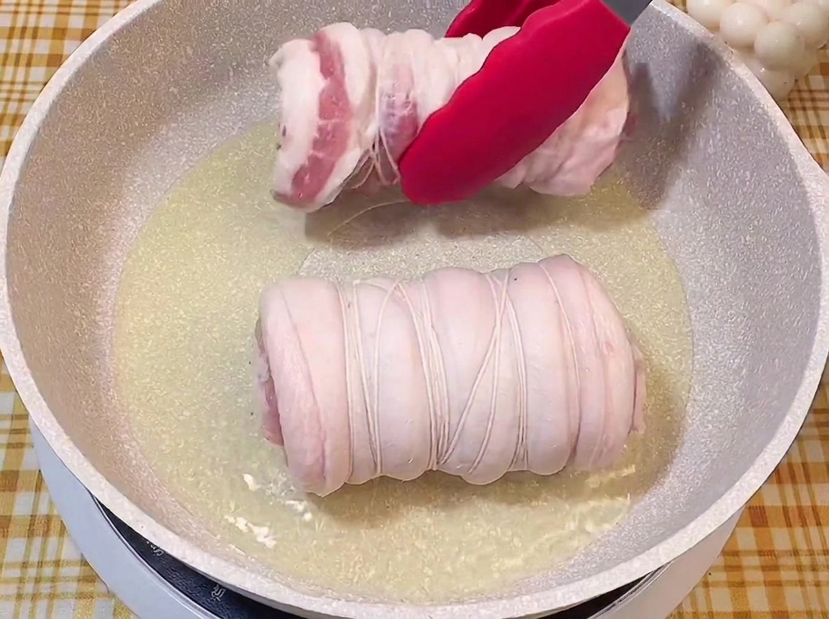 赤いトングを使って、熱したフライパンの油の中にタコ糸で縛った肉を入れる様子。