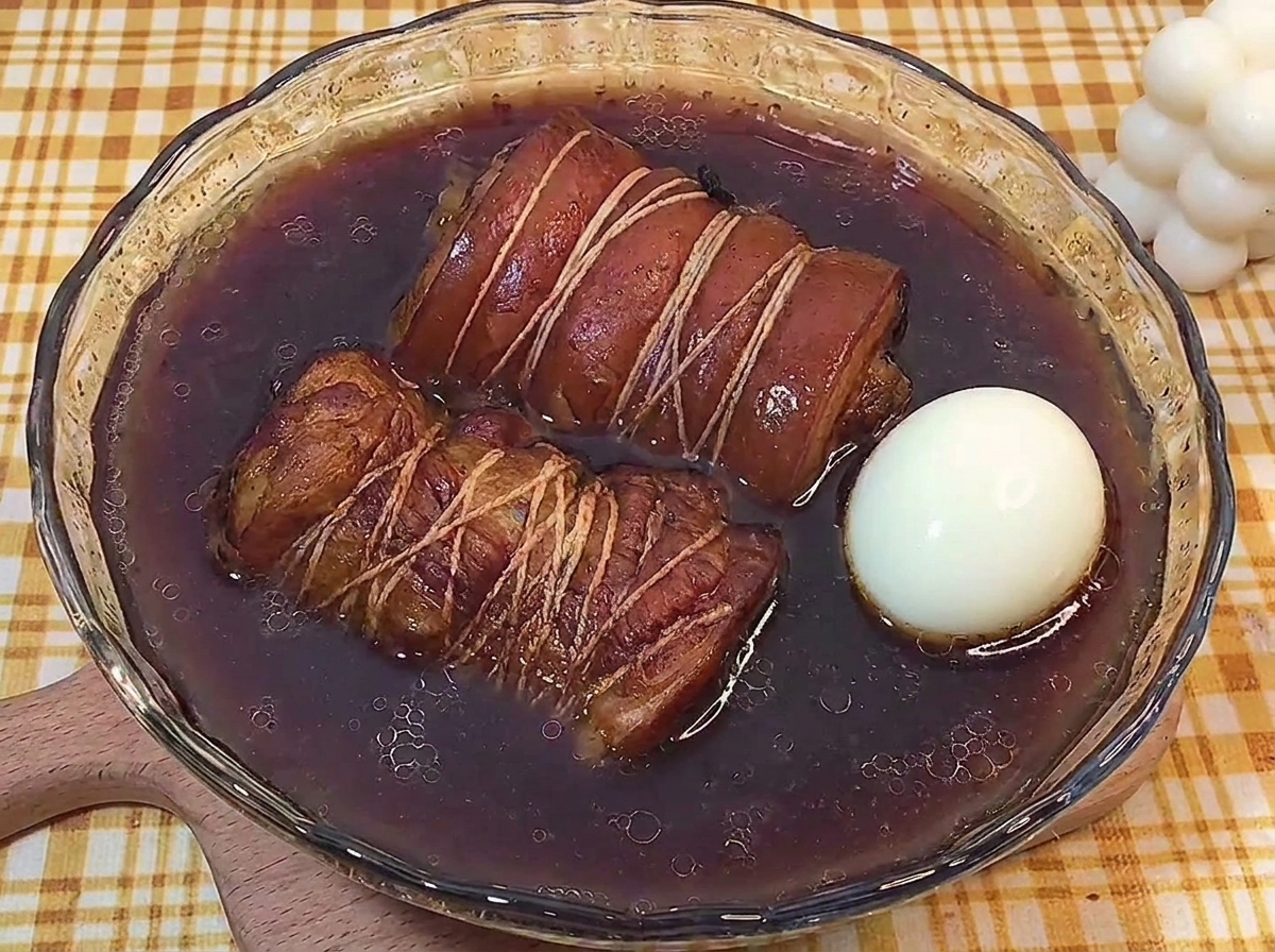 ガラスのボウルに入った濃い煮汁の中で、煮込まれた肉とゆで卵が浸かっている様子。