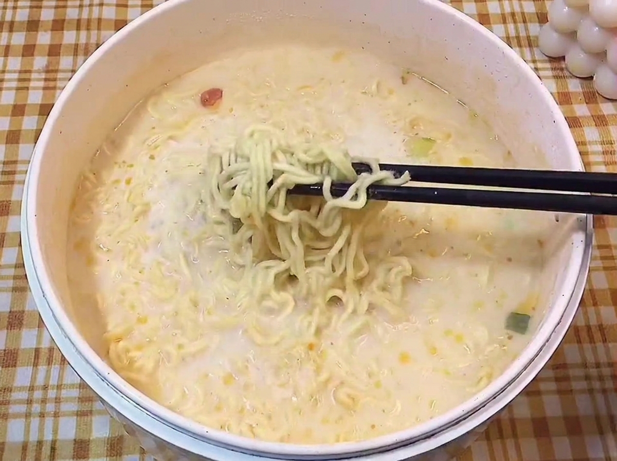 黒い箸で、白濁したクリーミーなスープからちぢれ麺を持ち上げている様子。