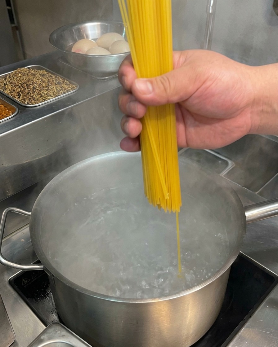 沸騰したお湯が入った鍋に、乾燥スパゲッティをパラパラと入れている様子。