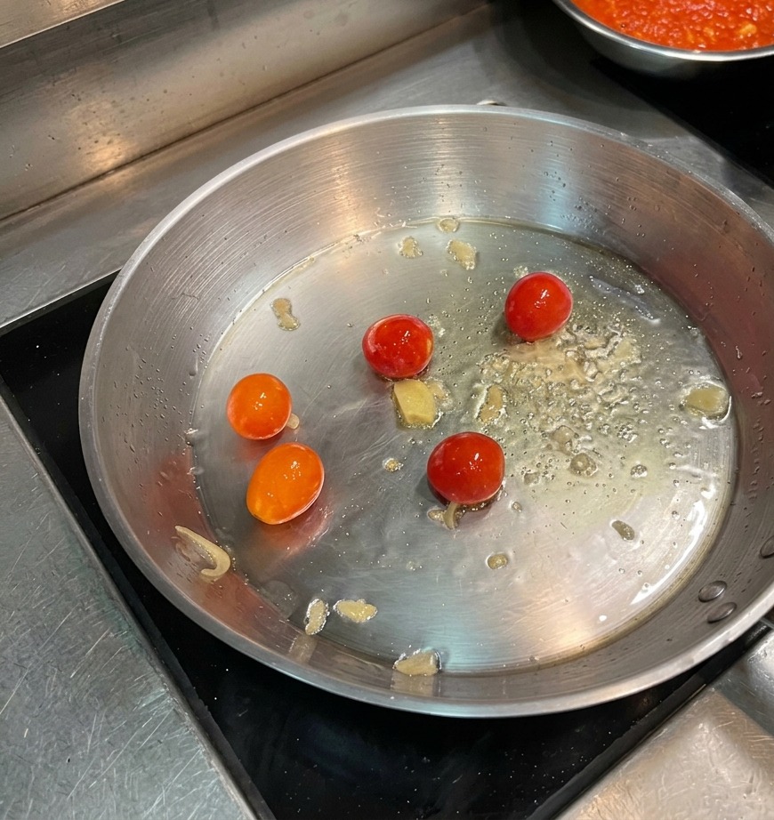 フライパンで焼かれているチェリートマトの上に、唐辛子フレークが散らされている様子。