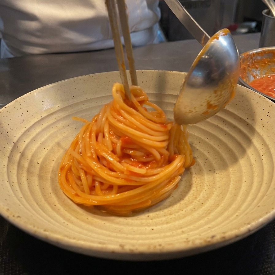トングとレードルを使い、お皿の上にスパゲッティを高く丸く盛り付けている様子。