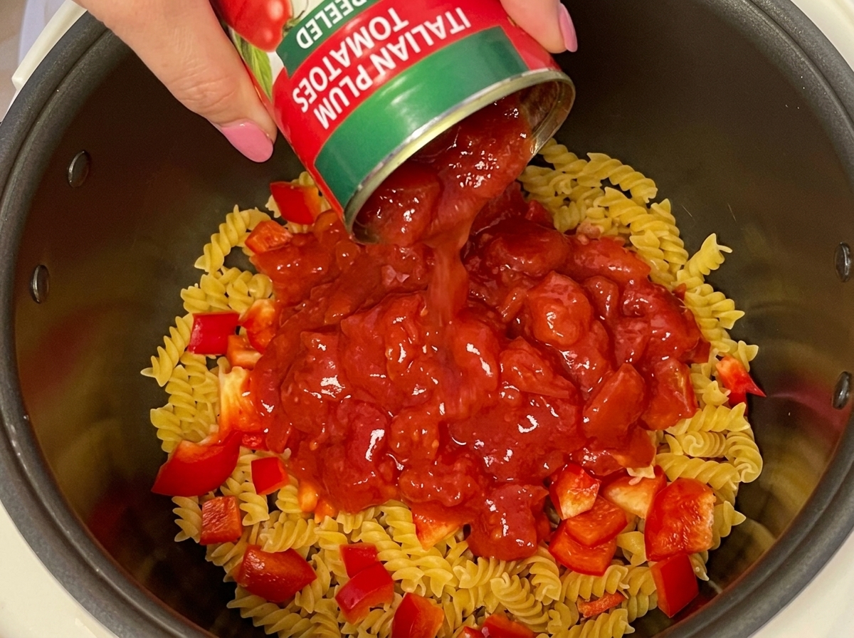パスタとパプリカの上にカットトマト缶を注いでいる様子。