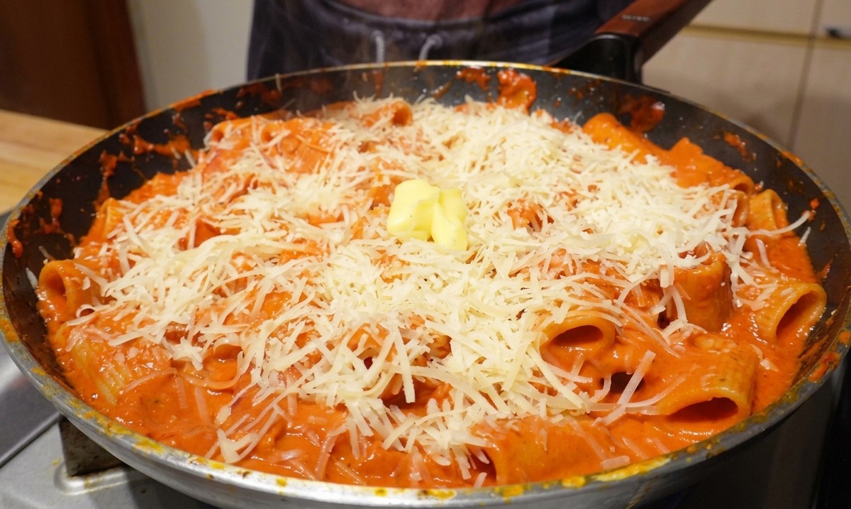 チーズとパスタが入ったフライパンの中央に、四角いバターが置かれている様子。