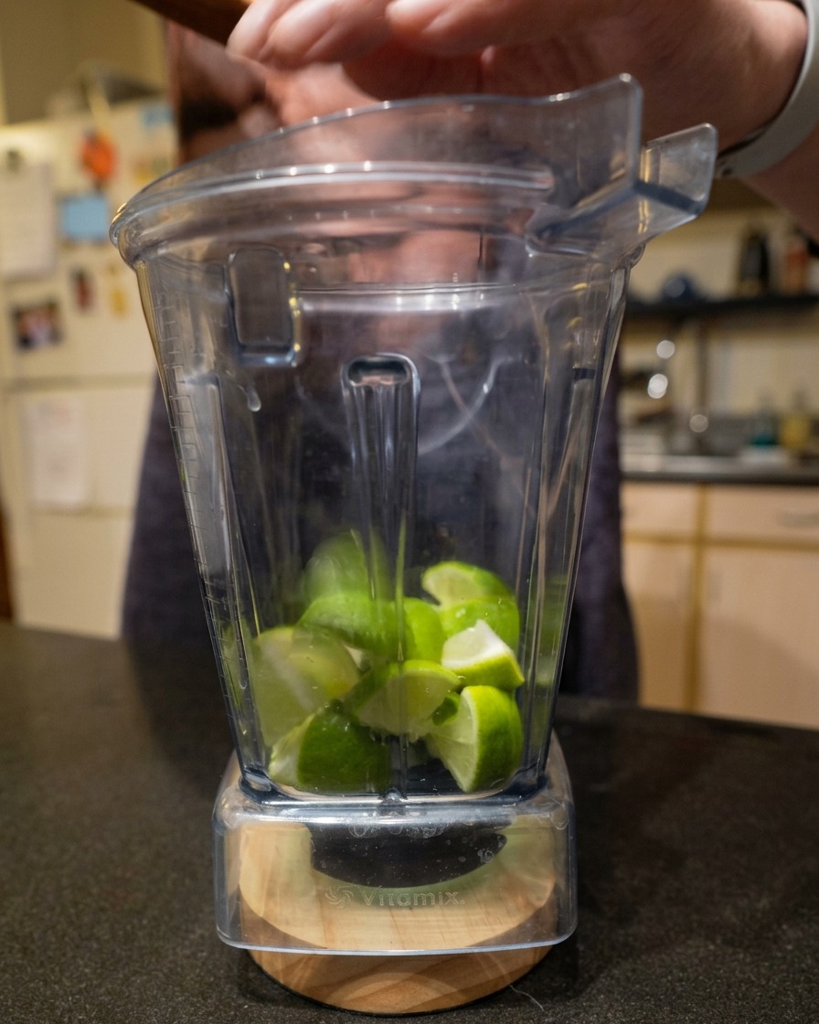 透明なミキサーの容器の中に、カットされた新鮮なライムが入っている様子。