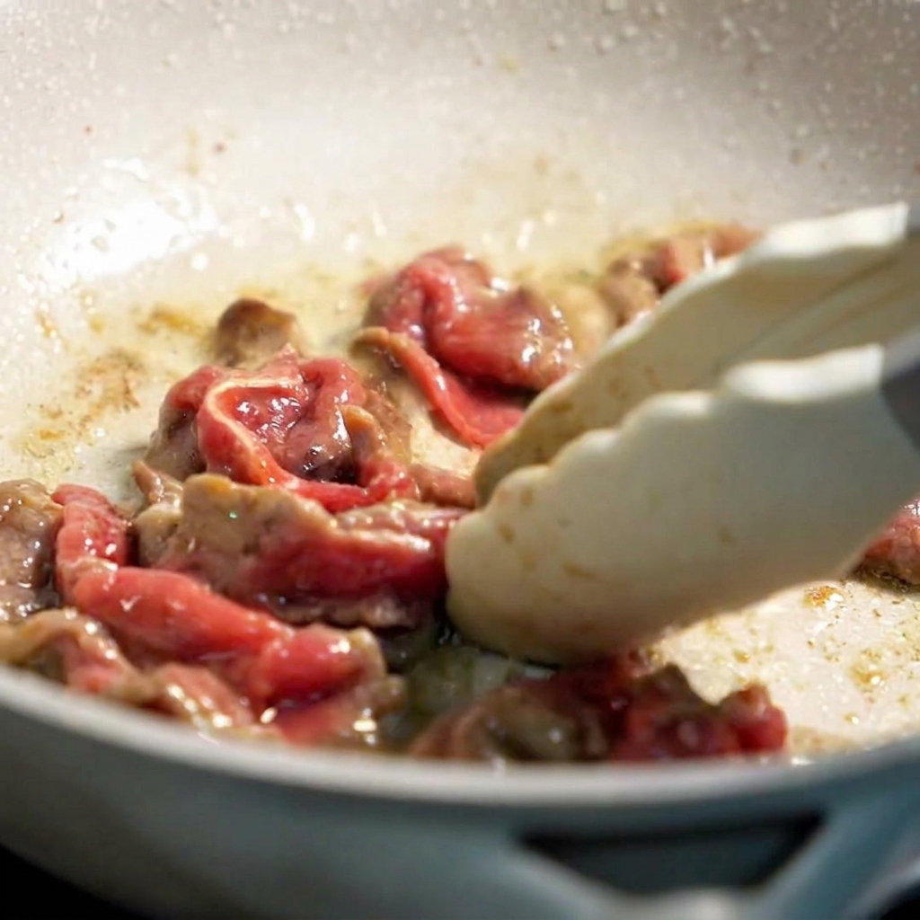 油を引いたフライパンで牛肉をトングで手早く炒めている様子。