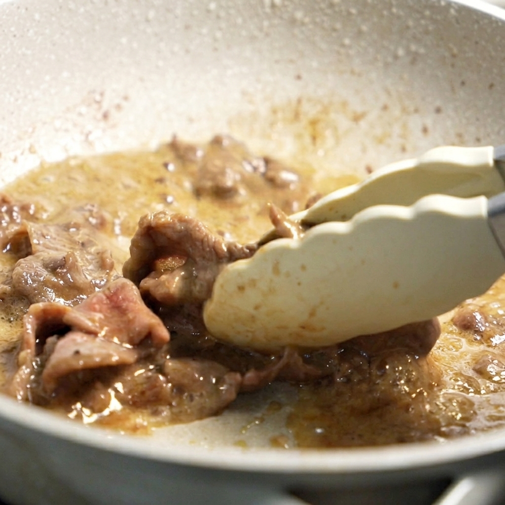 焼き色のついた牛肉をフライパンから取り出している様子。