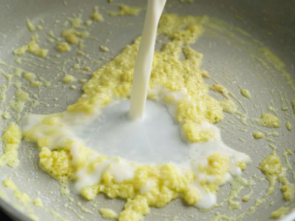 ニンニクを炒めたフライパンに、牛乳を細く注ぎ入れている様子。