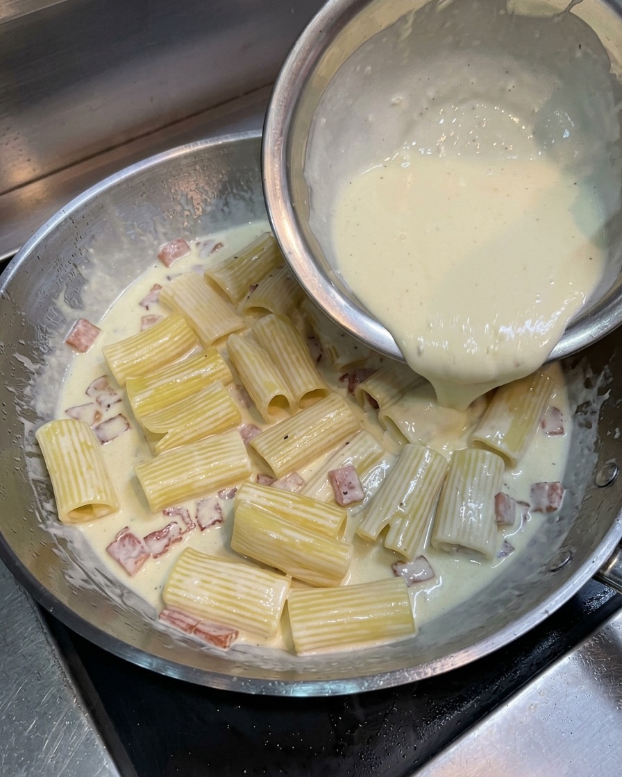 フライパンのパスタの上に、黄金色の卵液を回しかける様子。