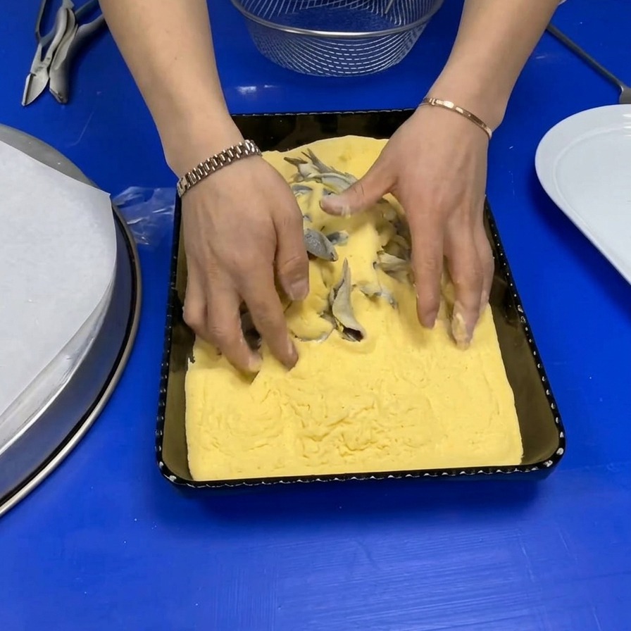 鮮やかなイエローコーンミールが入った長方形のバットの中で、新鮮な丸ごとのイワシに衣をまぶしているシェフの手。
