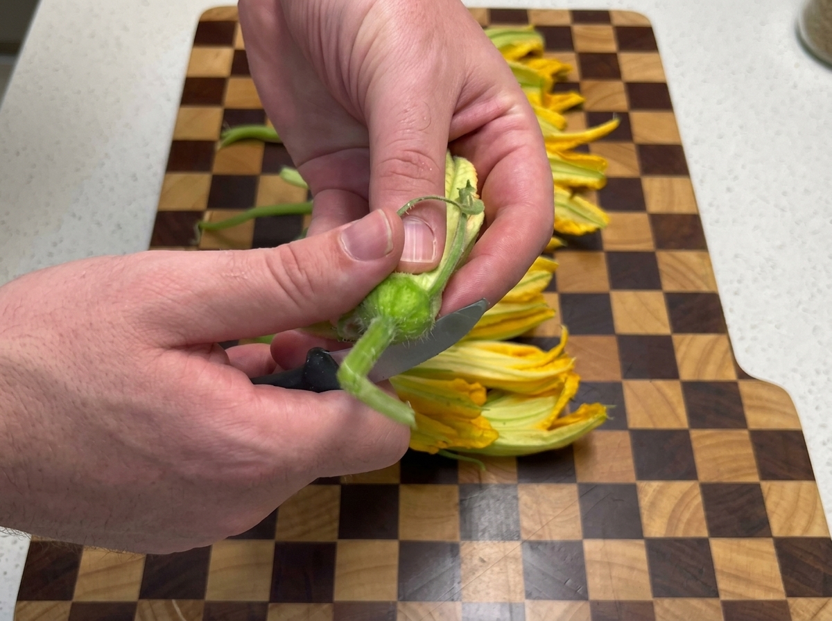木製のまな板の上で、ペティナイフを使ってカボチャの花の茎を切り落としている様子。