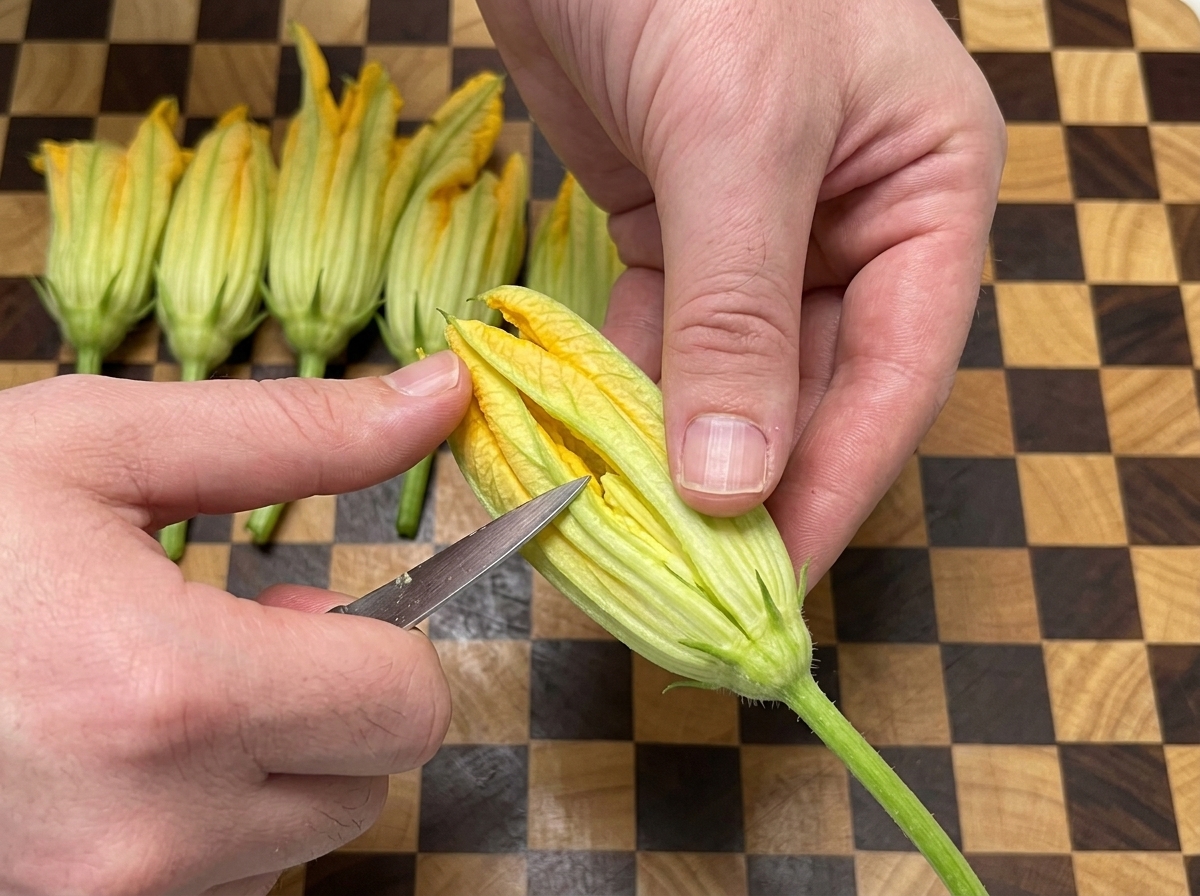 黄色のカボチャの花を持ち、ナイフで縦に切り込みを入れている手元。