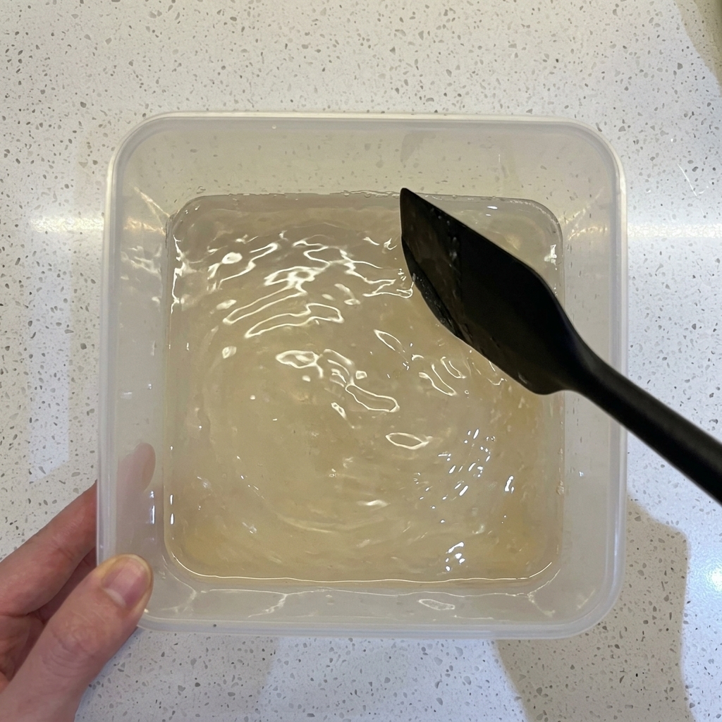 透明な容器の中で、水、小麦粉、イーストをヘラで混ぜ合わせている様子。