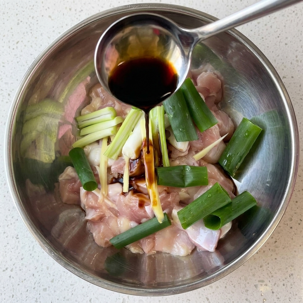 ボウルに入った鶏肉に醤油、ねぎ、生姜を加えて下味をつけている様子