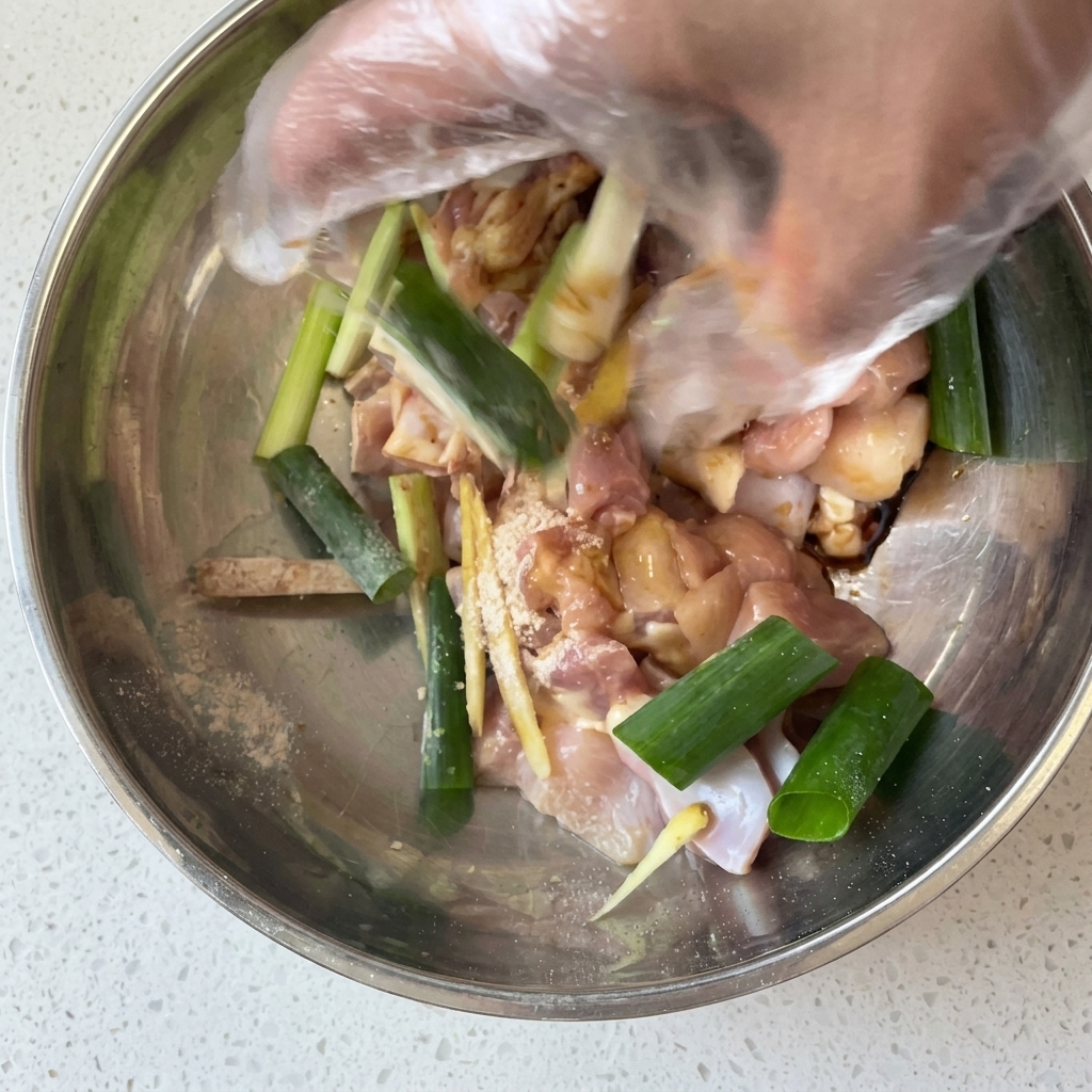 手袋をした手で鶏肉と調味料をしっかり揉み込んでいる様子