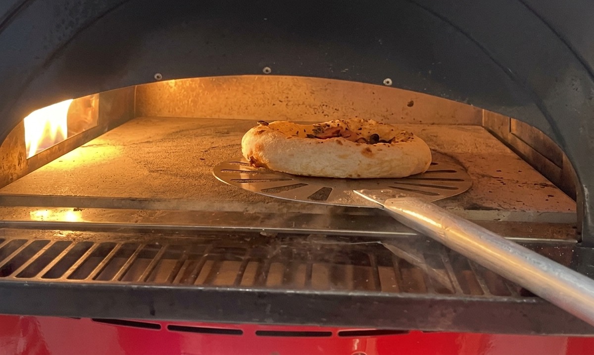 オーブンの中で縁が膨らみ、焼き色がつき始めたキノコとソーセージのピザ。