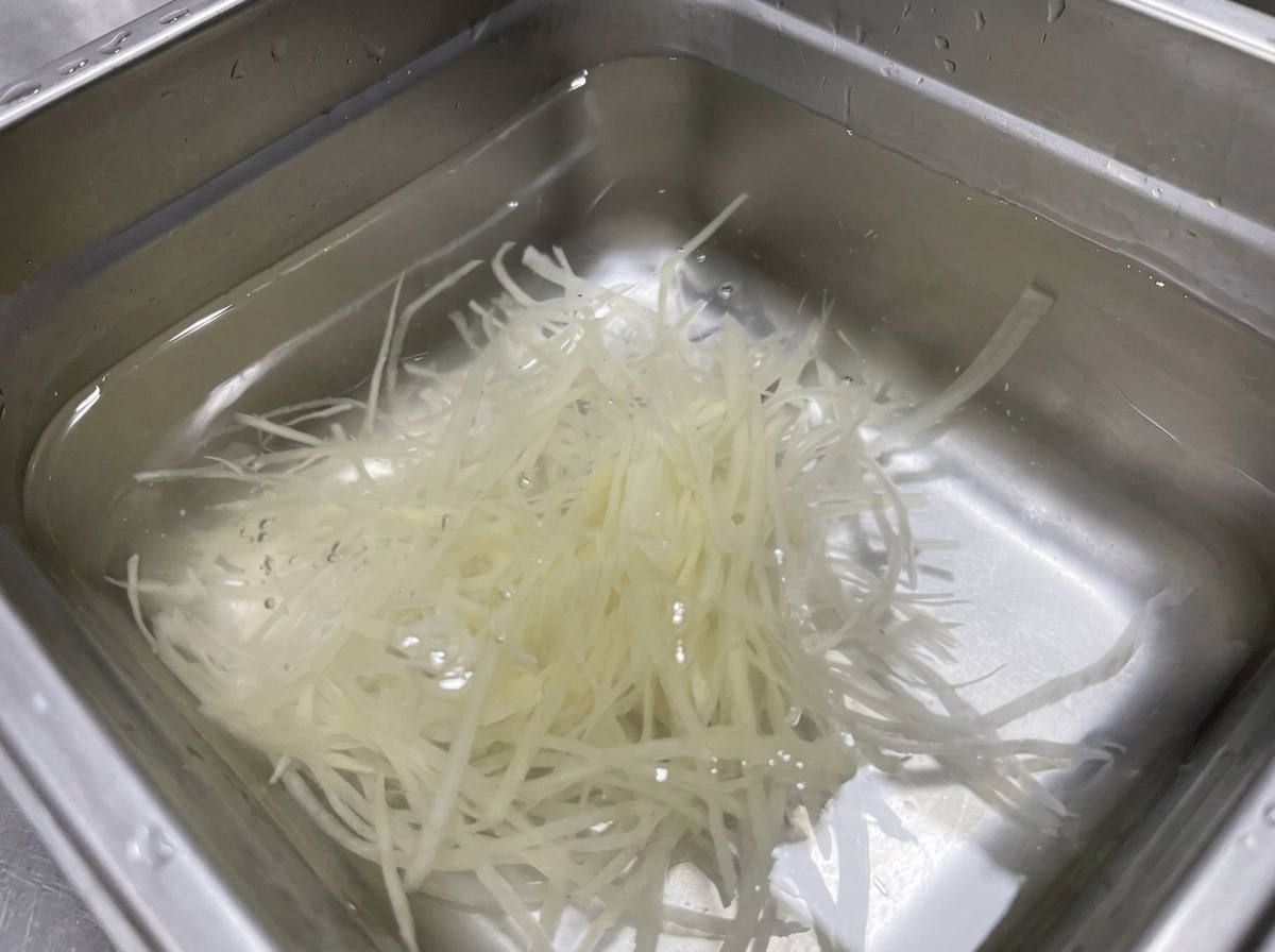 ボウルに張った透明な水の中に、千切りにしたじゃがいもを浸している様子。