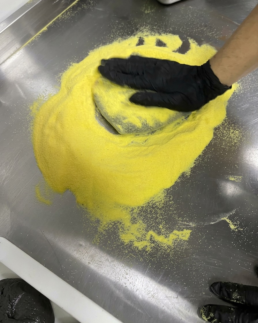 粉を振ったステンレスの作業台の上で、手袋をした手が黒い生地を円形に伸ばしている様子。