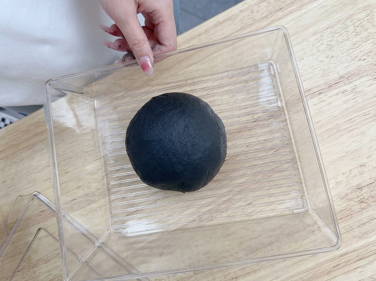 丸めた黒い生地を、プラスチックの保存容器に丁寧に入れている様子。