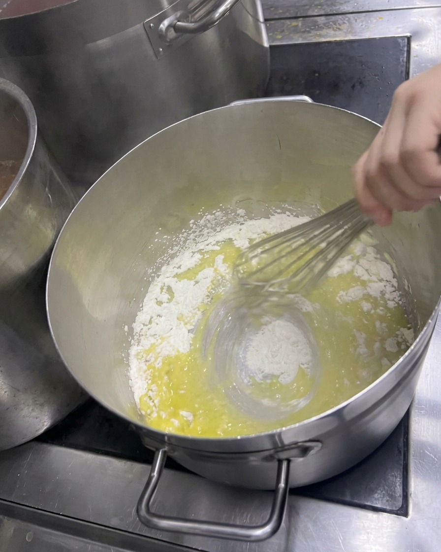 溶けたバターに小麦粉を加え、泡立て器で素早く混ぜて淡い黄色のペーストを作っている様子。