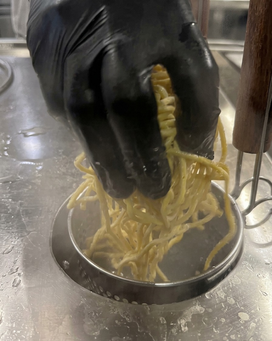 沸騰したお湯の中に、太い中華麺を投入している様子。