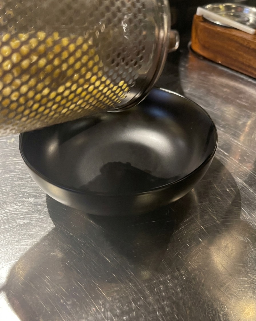湯切りした麺を、黒い器に盛り付けている様子。