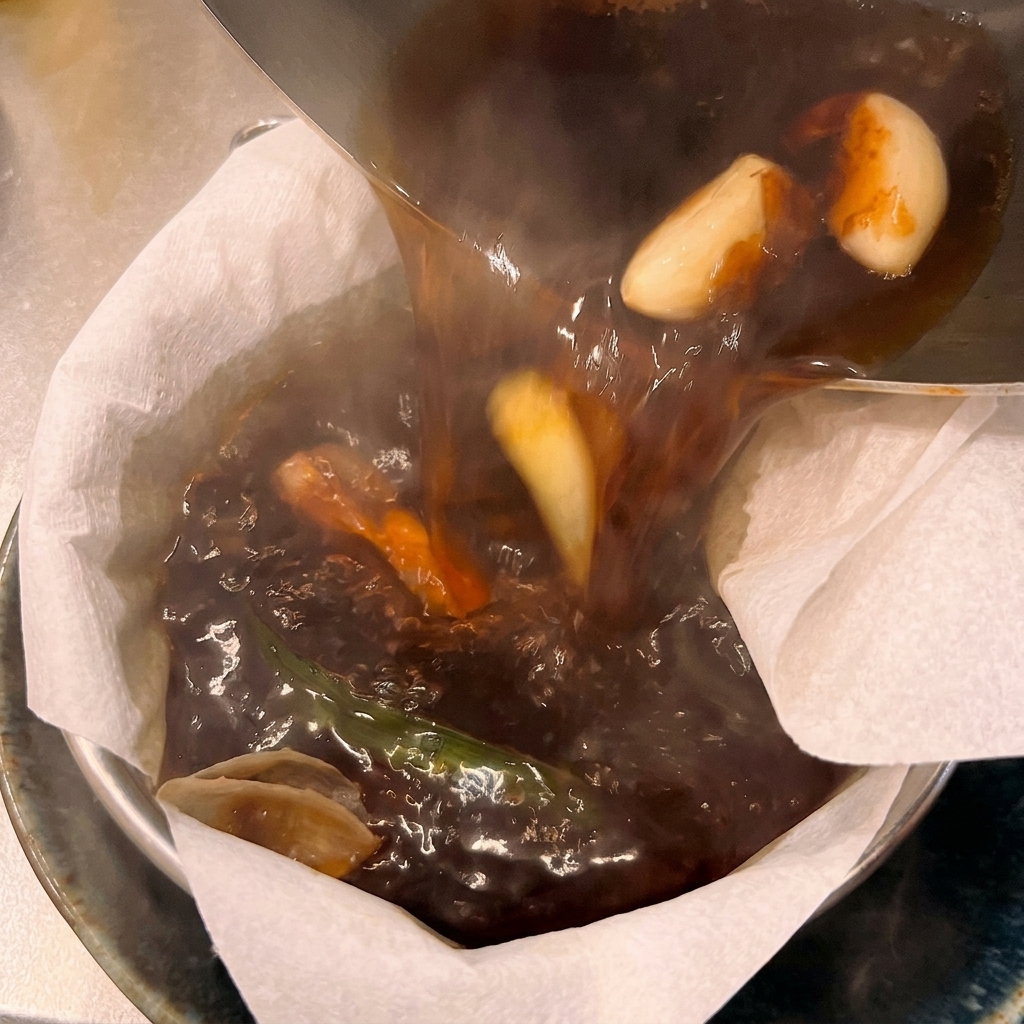 丼の上に置いたペーパーフィルターに、熱いラーメンスープを注いで濾している様子。