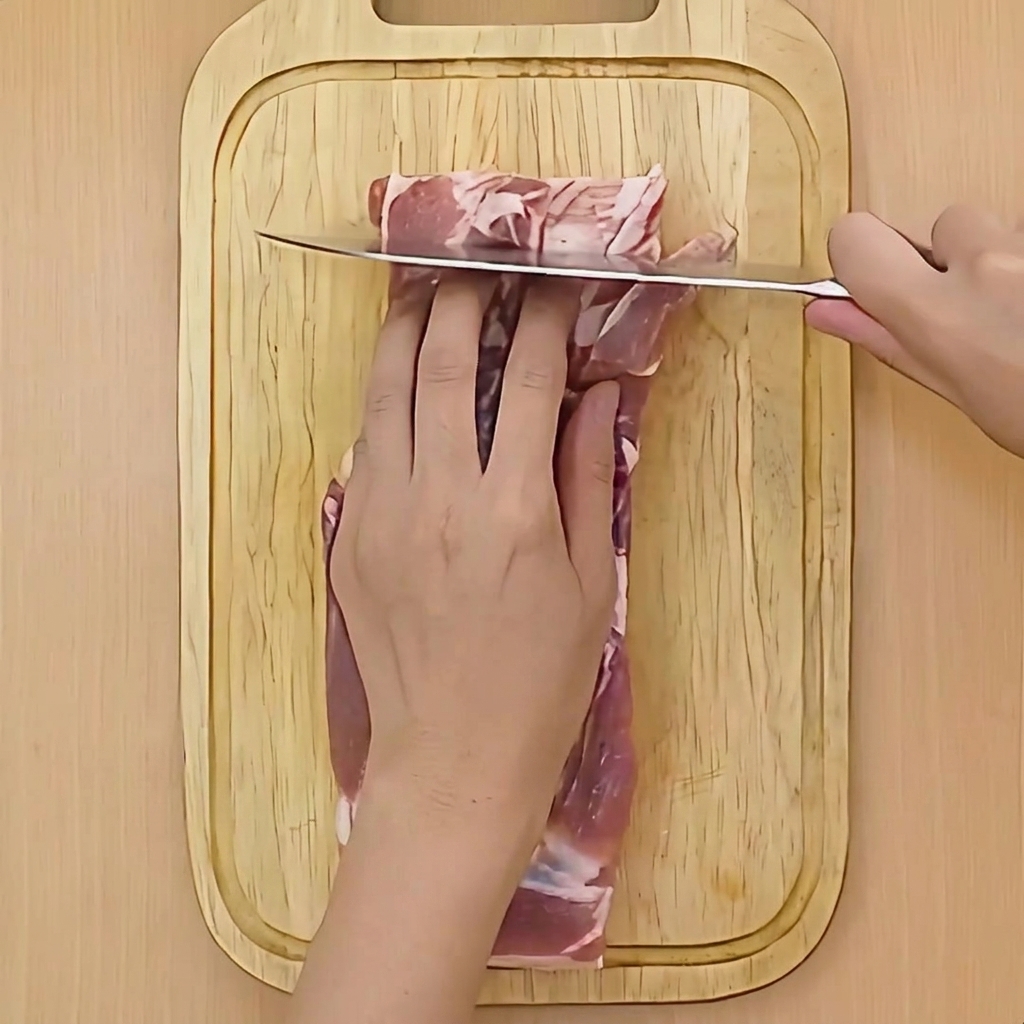 豚肉の表面に包丁で浅い切り込みを入れている手元。