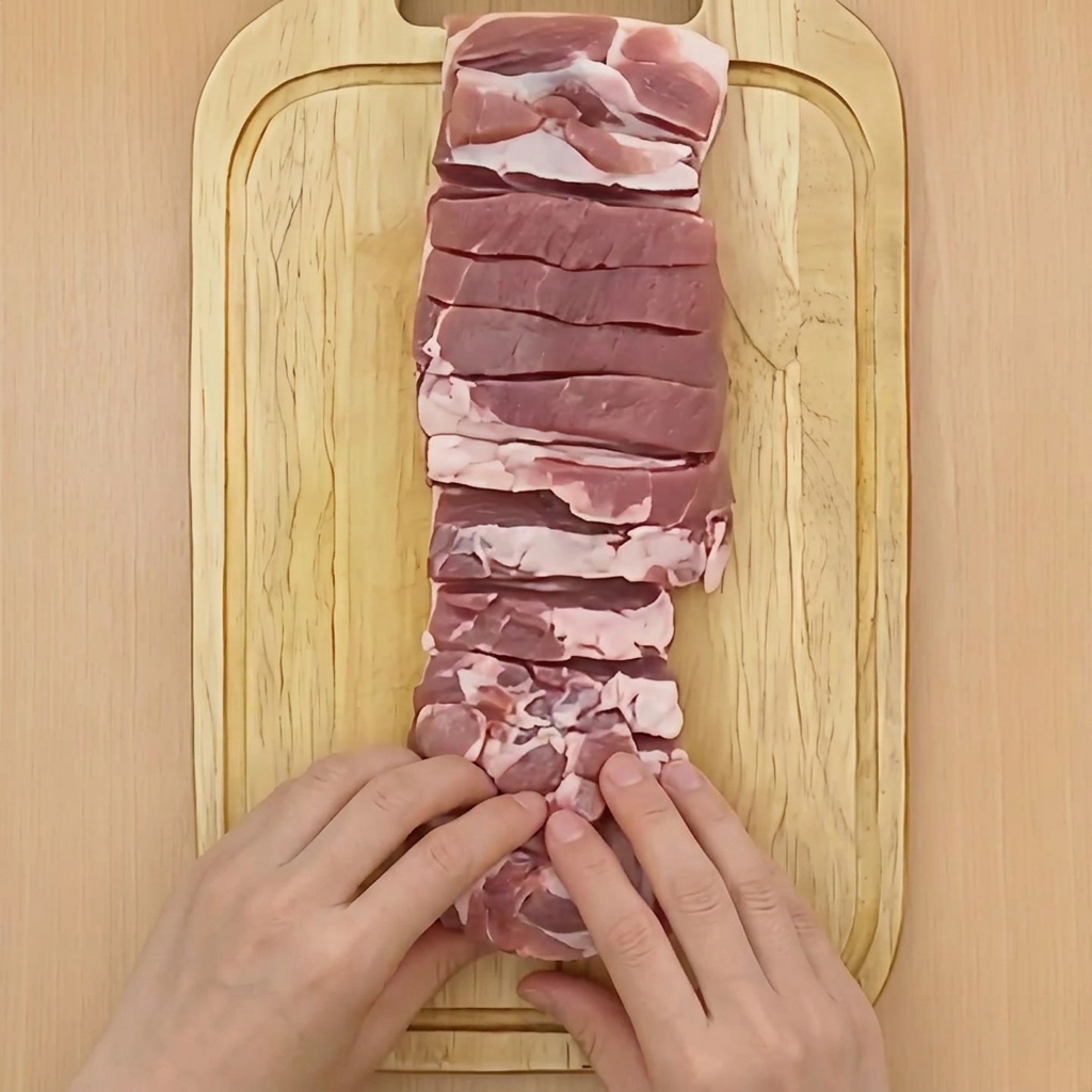 豚バラ肉を端からきつく円柱状に丸めている手元。