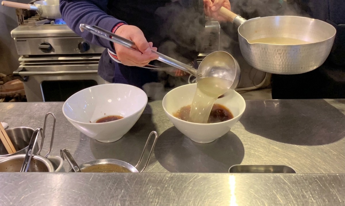 醤油タレが入ったどんぶりに、湯気の立つ透き通ったスープを注ぐ様子