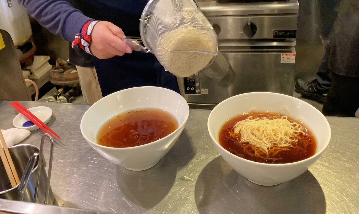茹でたての麺をザルから熱いスープの入ったどんぶりに移す様子