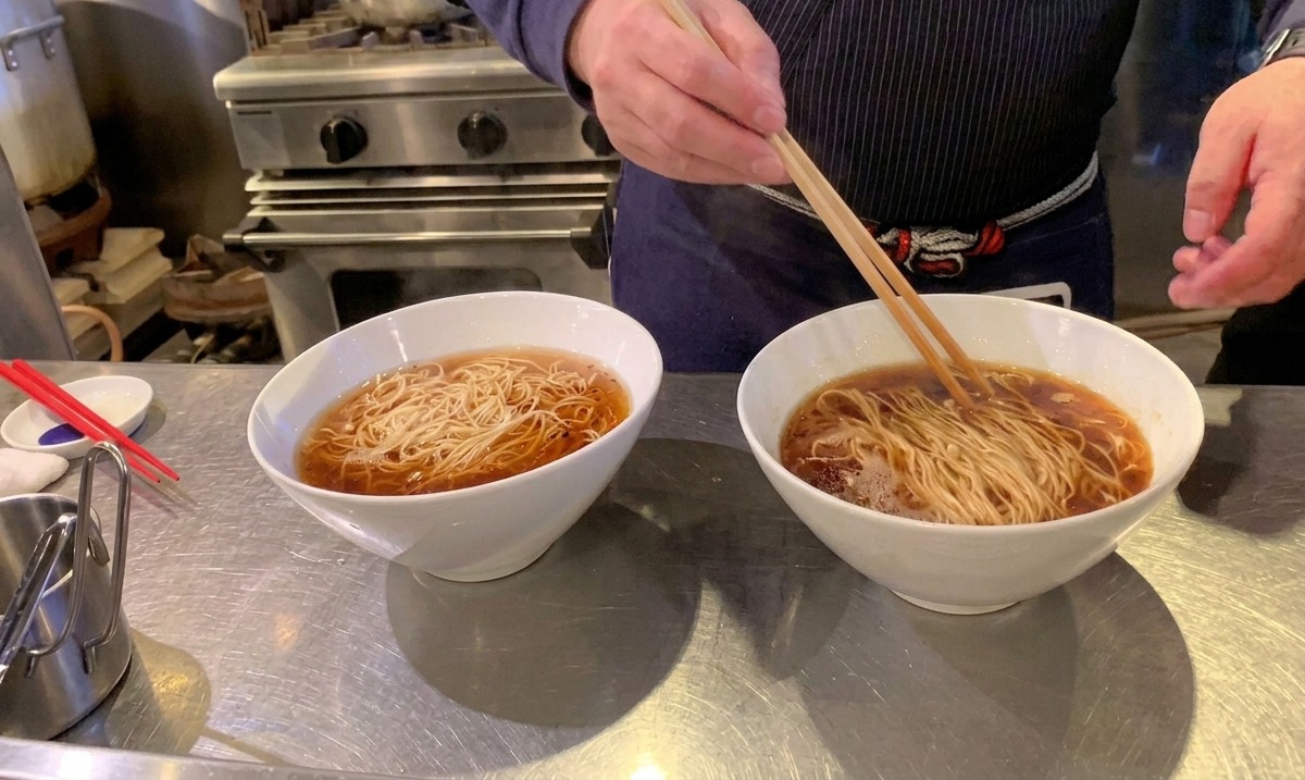 長い菜箸を使って、スープの中で麺をきれいに折り畳むように整える様子