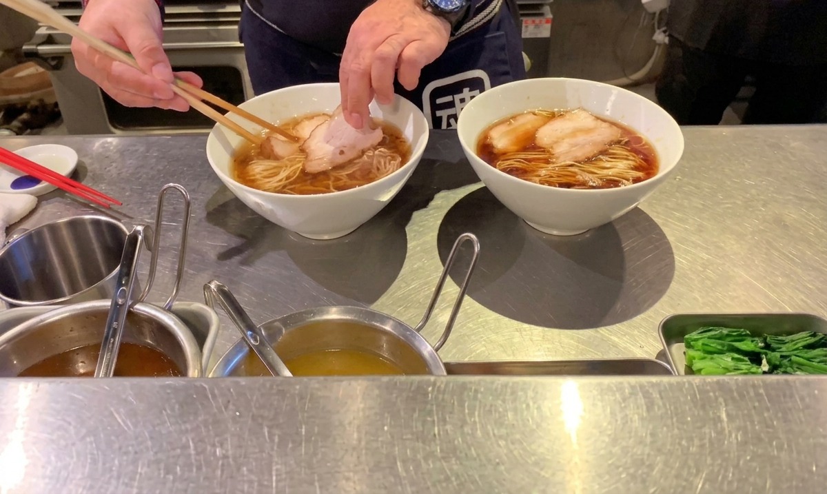 整えられた麺の上に、箸で豚チャーシューを丁寧に配置する様子