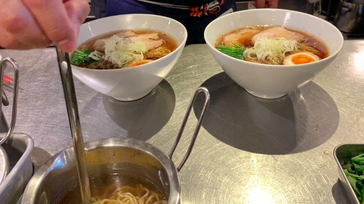 仕上げに小さなレードルで透明な香味油をラーメン全体にたらす様子