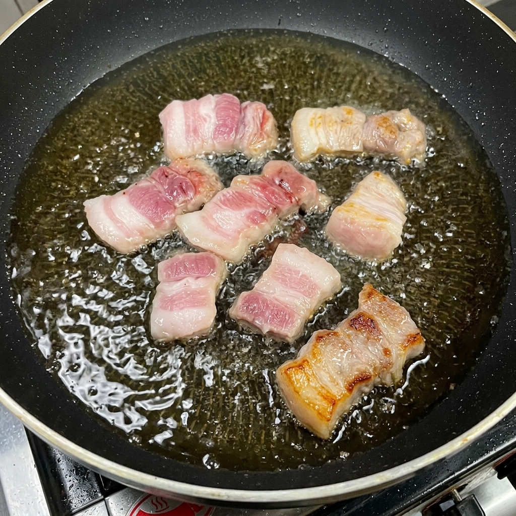 フライパンで豚バラ肉を焼き、脂が溶け出している様子。