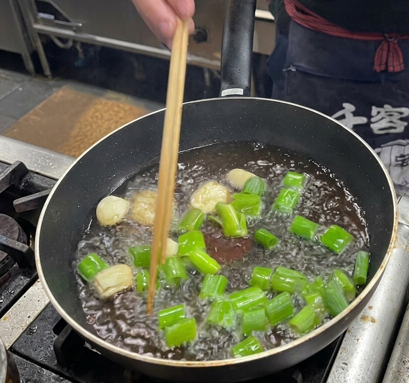 豚の脂が残ったパンで長ねぎ、にんにく、生姜を炒めている様子。